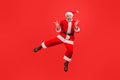 Full length portrait of happy elderly man with gray beard wearing santa claus costume jumping showing v gesture with fingers, Royalty Free Stock Photo