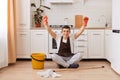 Full length portrait of happy handsome man sitting on the floor in kitchen with clenched fists, being happy to finish cleaning the