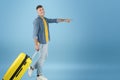 Full length portrait of happy male traveler with suitcase walking and pointing at empty space on blue studio background Royalty Free Stock Photo