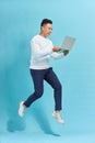 Full length portrait of happy man jumping and holding  laptop isolated over blue background Royalty Free Stock Photo