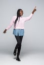 Full length portrait of a happy young african woman jumping and pointing finger at copy space over gray background Royalty Free Stock Photo