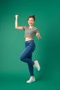 Full length portrait of happy young Asian woman standing on one leg and dancing on green background Royalty Free Stock Photo