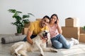 Full length portrait of happy young diverse couple with their dog posing on floor of new home on moving day Royalty Free Stock Photo