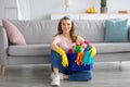 Full length portrait of happy young maid with bucket of cleaning supplies sitting on floor at living room Royalty Free Stock Photo