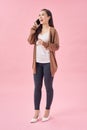 Full length portrait of a happy young woman talking on the phone isolated on a pinkbackground