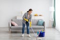 Full length portrait of happy young woman wiping floor in living room, copy space Royalty Free Stock Photo