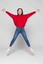 Full length portrait of a laughing woman in red sweater jumping over gray background Royalty Free Stock Photo