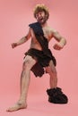 Full-length portrait of man in character of neanderthal wearing animal skin cloth and showing crazy movements isolated