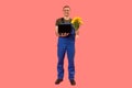 Full-length portrait of man in workers uniform holding laptop and bouquet of flowers, pink background. Copy space, mock up
