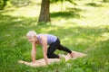 Full-length portrait of a middle-aged woman doing yoga or pilates on a mat in a park in plank pose with knee to hand.