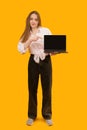 Full-length portrait of modern young woman holding laptop and pointing her index finger at blank black screen. Copy space, mock up Royalty Free Stock Photo