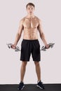 Full length portrait of motivated millennial bodybuilder exercising with dumbbells over light studio background