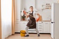 Full length portrait of positive optimistic dark haired Caucasian man wearing brown apron washing floor in kitchen having fun