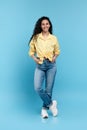 Full length portrait of positive young woman in trendy casual outfit standing and looking at camera over blue background