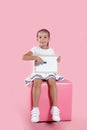 Full length portrait of a preschool little girl seated on chair holding and write on the board over pink backgrounds