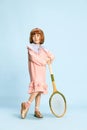 Full-length portrait of pretty little girl in pink dress posing with tennis racket against blue studio background Royalty Free Stock Photo