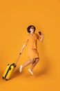 Full length portrait of pretty woman jumping with yellow suitcase. Happy girl traveler having fun