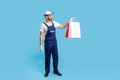 Full length portrait of professional courier in uniform giving shopping bags, looking serious responsible