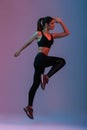 Full length portrait in profile of female fitness instructor wearing black tracksuit doing aerobics in gym, isolated over purple Royalty Free Stock Photo