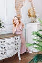 a full-length portrait of a red-haired woman in a silk dress leaning her elbow on an antique chest of drawers Royalty Free Stock Photo