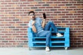 Full length portrait of shocked young bearded man in casual style and eyeglasses sitting on blue wooden pallet and pointing at Royalty Free Stock Photo