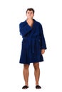 Full length portrait of sleepy young man messy hair, wears blue bathrobe yawning, covering his mouth with hand isolated on white Royalty Free Stock Photo