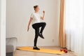 Full length portrait of slim athletic woman wearing white t shirt and black leggins doing sport exercises at home on yoga mat, Royalty Free Stock Photo