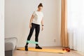 Full length portrait of slim sporty woman wearing white t shirt and black leggins doing sport exercises at home, standing and Royalty Free Stock Photo