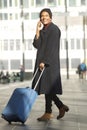 Full length smiling african american travel man walking in station with mobile phone and suitcase Royalty Free Stock Photo