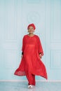 Full length portrait of smiling African woman dressed in stylish traditional ethnic red suit and head scarf, posing on