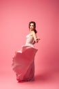 full-length portrait of smiling dark-haired woman in long pink evening dress, with skirt flying in motion,  on Royalty Free Stock Photo