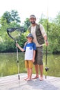 Full length portrait of smiling father and son  standing with fishing  tackles on pier against lake Royalty Free Stock Photo