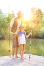 Full length portrait of smiling father and son  standing with fishing  tackles on pier against lake Royalty Free Stock Photo