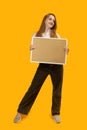 Full-length portrait of smiling young woman with note board or cork board, yellow background. Copy space