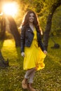 Full length portrait of a girl with long hair, in a jacket and dress in the park,, against the background of the sunset Royalty Free Stock Photo