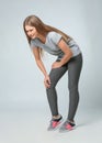 Full length portrait of sportswoman having knee problems on grey