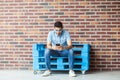 Full length portrait of successful handsome young bearded man in casual style, eyeglasses sitting on blue wooden pallet, holding, Royalty Free Stock Photo