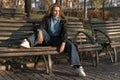 Full-length portrait of teenage girl in casual style in wide jeans sitting on bench in an autumn park. Sunny day Royalty Free Stock Photo