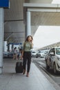 Full length portrait of traveling young woman with suitcase outside the airport