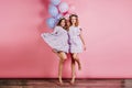 Full-length portrait of two barefooted ladies having fun at party. Indoor photo of caucasian girls in dresses dancing