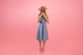 Full length portrait of unrecognizable young lady covering face with bouquet of flowers on pink background, copy space Royalty Free Stock Photo