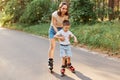 Full length portrait of woman and little son rollerblading together, mother teaching to roller skate his child, cute boy learning Royalty Free Stock Photo