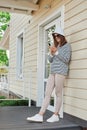 Full length portrait of woman wearing striped shirt using phone on porch of house reading news in internet scrolling online