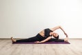 Full length portrait of young adult woman in black pants and toppracticing yoga, siting on splits and doing revolved head to knee Royalty Free Stock Photo