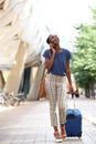 Full length young african american woman walking in city with luggage and talking on mobile phone Royalty Free Stock Photo