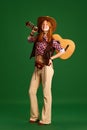 Full-length portrait of young attractive girl, teenager dressed retro cloth and posing with guitar against green studio Royalty Free Stock Photo