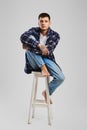 Full length portrait of young barefoot man in shirt and jeans sitting on tall wooden chair Royalty Free Stock Photo