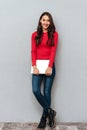 Full length portrait of young beautiful woman in casual wear holding laptop, looking at camera Royalty Free Stock Photo