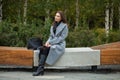 Young beautiful woman in a gray coat sitting on a bench in the autumn park Royalty Free Stock Photo