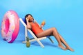 Full length portrait of young black woman chilling in lounge chair with yummy tropical cocktail on blue background Royalty Free Stock Photo